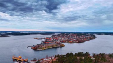 Kuzey Avrupa 'da deniz kenarındaki küçük bir ada kasabası bulutlu gökyüzünün altında. Suyla çevrili bir adada küçük bir kasaba var. Yakınlarında tekneler ve bulutlu gökyüzünün altında binalar var..