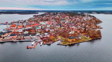 Gün ışığında binaların, suyun ve teknelerin kıyı manzarası. Açık bir günde kıyıya yanaşmış teknelerle çevrili bir adada pek çok bina var..
