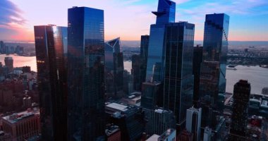 ABD 'nin New York şehrinde çeşitli şekillerde cam gökdelenler. Gökyüzü ve su manzarası gün batımında turuncu renktedir..