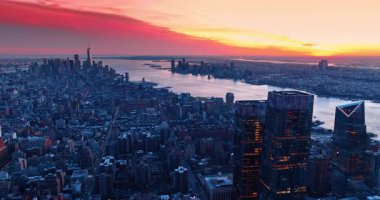New York, ABD 'nin engin panoramasının üzerinde parlak pembe ve turuncu bir gökyüzü. Alacakaranlıkta nehir kıyısındaki şehir manzarasına iniyoruz..