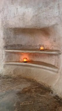 Mağarada yaratılan raflarda iki mum yakıldı. Taşa kazınmış bir duvar. Dikey video.