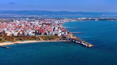 Türkiye 'de güneşli bir günde deniz kenarındaki bir kasabanın kıyı manzarası. Türk kıyı kasabasında kıyı şeridi boyunca uzanan renkli binalar nedeniyle insanlar plajın keyfini çıkarıyor.