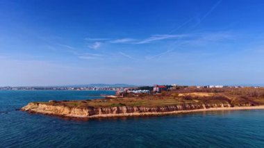 Kıyı şeridi manzaralı deniz manzaralı binalar ve doğa uzaklarda. Açık mavi gökyüzünün altında görünen binalar ve yeşilliklerle denize doğru uzanan bir kara parçası..