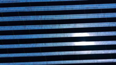 Güneş panelleri güneş ışığı altında düz bir yüzeyde sıra sıra dizilmiş. Güneş panellerinin sıraları, yukarıdaki güneşten yansıyan ışığı yansıtan düz bir yüzeye kurulmuştur..