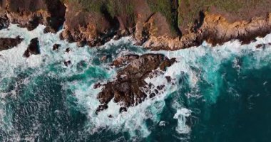 Güçlü köpüklü dalgalar kayalara çarpıyor. Güneşli bir günde okyanusun kayalık kıyılarına iniyor..