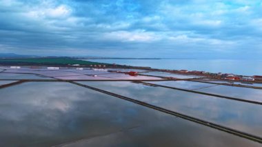 Tuz üretimi için tuz tarlaları üzerinde uçuyorlar. Bazı evler deniz kıyısında. Yoğun bulutlar gökyüzünü kaplıyor.