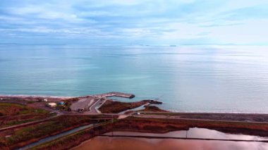 Güzel mavi su manzarası bulutlu gökyüzü ile birleşiyor. Tuz madenciliği için pembe göletler üzerinde İHA uçuşu.