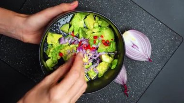 Salsa ya da sos hazırlamak için taze avokado ve soğanı bir kasede karıştırıyorum. Eller, bir kase doğranmış avokado ve soğanı mutfak tezgahında salsa ya da sosa hazırlarken tutsun..