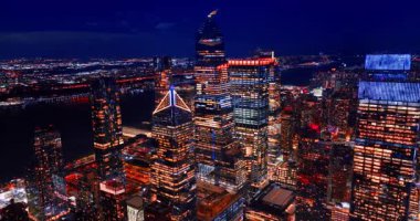 Pencereleri açık olan güzel gökdelenlerden oluşan bir grup. Nehrin arka planında karanlık bir bölge. New York, ABD Geceleri.