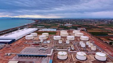 Deniz kıyısındaki modern petrol rafinerisi fabrikası. Arkaplanda bulutlu gökyüzü altında geniş şehir manzarası. Hava görünümü.