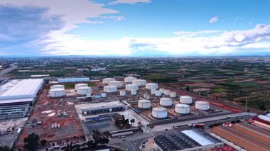 Yakıt depolamak için çeşitli büyüklükteki tankları olan modern bir petrol rafineri fabrikasının geniş bir bölgesine yaklaşıyoruz. Hava görüntüsü. Arkaplanda yeşil alanlar ve geniş şehir manzarası.