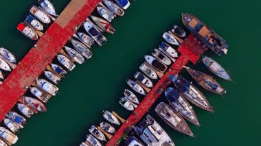 Sıraya dizilmiş gemilerle iki rıhtımın üzerinde daireler çiziyorlar. Limanda çeşitli tekneler var..