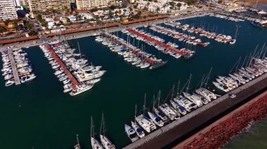 Büyük ve küçük tekneler deniz yeşili su manzarasındaki rıhtımlarda dururlar. Birçok villa ve palmiye ağaçlarıyla rıhtıma yaklaşıyorlar..