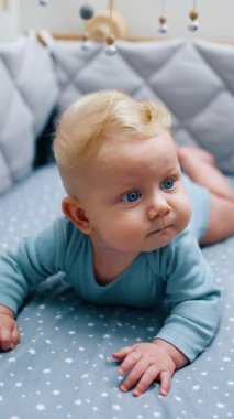 Mavi elbiseli şirin mavi gözlü bebek karnının üstünde yatıyor. Beşiğinde sevimli bir çocuk var. Dikey video