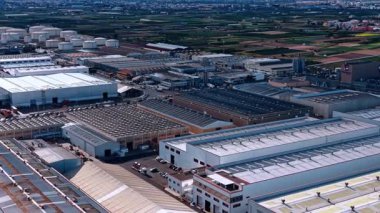 Endüstriyel bölgede büyük depolar. Arka plandaki fabrikada yuvarlak tanklar var. Hava görünümü.