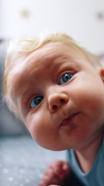 Şirin, tombul, beyaz bir bebeğin tatlı yüzü. Kapatın. Beşikte karnının üstünde yatan sevimli bir bebek. Dikey video