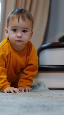 Turuncu spor takım elbiseli şirin bebek dördü de yerde dikilip önüne bakıyor. Çocuk tatlı tatlı gülümsüyor ve kameraya doğru sürünüyor. Dikey video