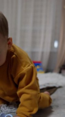 Ağzında emzik ile yerde oturan güzel bir bebek. Çocuk sakinleştiriciyi gevşetiyor, alıyor ve ağzına çekiyor. Dikey video