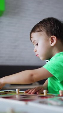 Siyah saçlı, açık tişörtlü çocuk masasında oyuncaklarıyla meşgul. Bulmaca toplayan sevimli bir çocuk. Dikey video