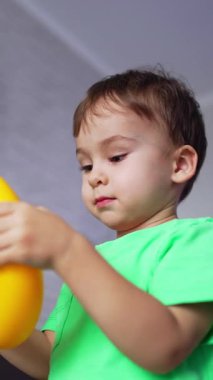 Sevimli çocuk piramidin yüzüğünü direksiyon simidi olarak kullanarak elinde tutuyor. Küçük çocuk oyuncağı koluna taktı ve yere düştü. Düşük açı. Dikey video