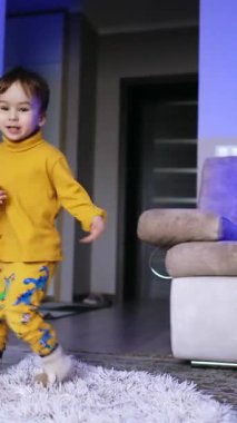 Neşeli çocuk enerjik bir şekilde adımını atıyor ve dönüyor. Mutlu çocuk ekose kumaşın üstüne düşüp yuvarlanıyor. Düşük açı. Dikey video