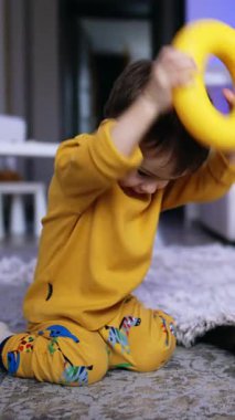 Sarı kazaklı sevimli kahverengi saçlı bebek oyuncak yüzüğü kafasına takıyor. Evde oynayan komik çocuk. Dikey video