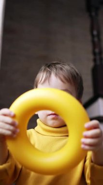 Gülümseyen siyah saçlı bebek kafasına piramit yüzüğü takıyor. Çocuk oyuncağı düşürür ve sevimli bir şekilde gülümser. Düşük açı. Dikey video