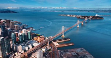 Oakland Bay Köprüsü 'ne yaklaşıyoruz. Mavi deniz manzarası üzerinde hareketli bir trafik var. Rıhtımdaki yüksek binaların hava manzarası. San Francisco, California, ABD.