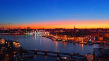 İsveç, Stockholm 'ün tarihi merkezinden akşam vakti güzel bir aydınlanma ile uzaklaşıyor. Rıhtımlarda birden fazla tekne ile nehir üzerinde uçmak.