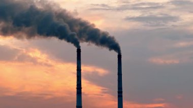 Akşam gökyüzünde gün batımında bir fabrikada bacalardan duman yükselir. Fabrikadaki bacalar gün batımında gökyüzüne duman salıyor.