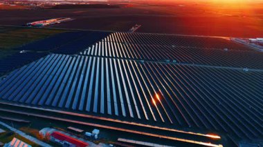 Uzun güneş panelleri batan güneşe döndü. Arabalar tarımsal tarlalar boyunca arka planda otoyolun yanından geçiyor. Hava görünümü.