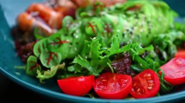 Sağlıklı salata ve taze malzemeler öğle vakti mavi tabakta servis edilir. Bir kasede taze sebzeler, domatesler ve mavi tabakta soslu ızgara balık parçaları var..