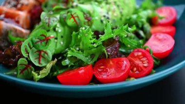 Mavi tabakta servis edilen taze salata, kiraz domatesleri ve somon. Bir tabakta yeşil salata, kiraz domatesleri ve renkli bir yemek oluşturan somon parçaları var..