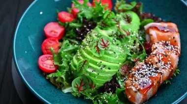 Mavi tabakta servis edilen somon, avokado ve kiraz domatesli sağlıklı salata. Taze salata, somon, avokado, kiraz domatesleri ve öğle yemeği için mavi tabakta yeşiller..