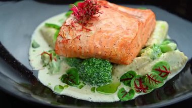 Restoran ortamında sebze ve sosla servis edilen somon tabağı. Bir tabak, kremalı soslu sebze yatağında pişmiş somon tutar..
