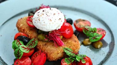 Lezzetli bir yemek, kızarmış bir şey, domates ve gri bir tabakta otlar. Çeri domatesler ve yeşilliklerle çevrili haşlanmış yumurtayla kaplı bir tabakta..