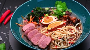 Mavi bir kasede yumurta ve sebzeli erişte çorbası. Bir kase erişte, dilimlenmiş et ve sebzeli haşlanmış yumurta ve otlar içerir..