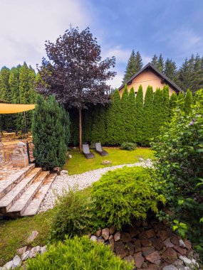 Dağın eteklerindeki yeşil avlu. Dağlık bir bölgede ağaçlar ve şezlonglar olan yeşil bir avlu.