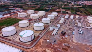 Geniş petrol rafineri tesisi üzerinde çeşitli tanklarla uçmak. Arkaplanda tarım tarlaları ve kentsel alan.