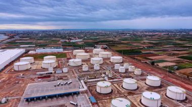 Kimya fabrikasındaki depolama tanklarının görüntüleri. Tarım alanları ve şehir manzarası yukarıdaki bulutlu gökyüzü altında.