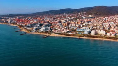 Sahil şeridinin geniş bir görüntüsü, tatil köyleri ile birlikte. Arka planda oteller, plajlar ve yeşil tepelerin yer aldığı panoramik deniz manzarası.