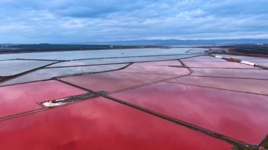 Parlak pembe tuz tavaları ve makinelerden oluşan hava manzarası. Pembe göletler arasında dar bir baraj üzerinde ağır makinelerle tuz çıkarma alanının ayrıntılı görüntüsü.