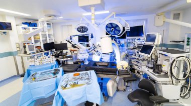 Görüntüleme sistemleri ve cihazları olan yüksek teknoloji nörocerrahi süiti. Çeşitli çalışma istasyonlarını gösteren bir ameliyathane, C-kolu röntgeni, cerrahi monitörler, ve nörocerrahi aletlerle hazırlanmış masalar. Parlak, steril bir çevre.