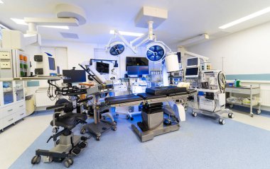Dijital görüntüleme ekranlı modern cerrahi tiyatronun içi. Çok sayıda monitörü, ameliyat ışıkları ve mobil tıbbi çalışma istasyonları olan yüksek teknolojili bir hastane odasına genel bakış.