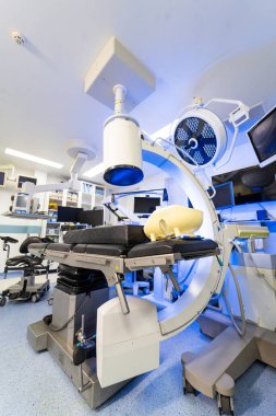 Ameliyat masasının üzerinde C-kolu floroskopi sisteminin dikey görüntüsü. Modern bir hastane ameliyathanesinde tıbbi görüntüleme ekipmanları ve cerrahi ışıkların üst perspektifi.