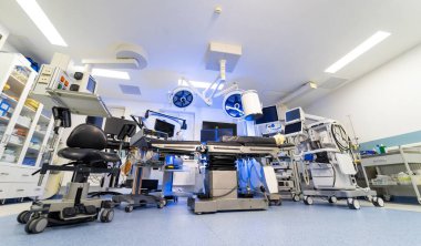 Modern müdahale radyolojisi ve cerrahi süitine kapsamlı bir bakış açısı. C-kolu, tıbbi malzeme dolapları ve karmaşık işlemler için kapsamlı izleme ekipmanlarını gösteren boş bir ameliyathanenin geniş perspektifi.