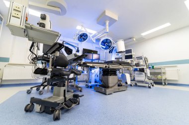 Mobil görüntüleme ve monitörlerle gelişmiş cerrahi odası. C-kolu floroskopi sistemi, cerrah koltuğu ve tavana monte medikal monitörleri olan modern bir tıbbi süitin perspektif görüntüsü.