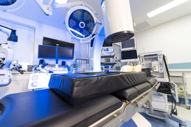 Hastanedeki hasta masasının üzerinde cerrahi C-kolu sistemi var. Modern bir klinik ameliyathanede tıbbi görüntüleme ekipmanları ve cerrahi ışıklar..