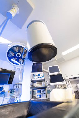 Modern cerrahi tiyatroda robot X-ray C-kolu. Yüksek teknolojili bir hastane odasında tıbbi görüntüleme cihazları ve monitörlerin detaylı görüntüsü..