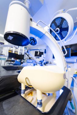 Röntgen cihazı ve nöroşirürji odasında cerrahi ışıklar. C-kolu floroskopi sisteminin düşük açılı görüntüsü ve steril çalışma odasındaki cerrahi LED ışıklar..